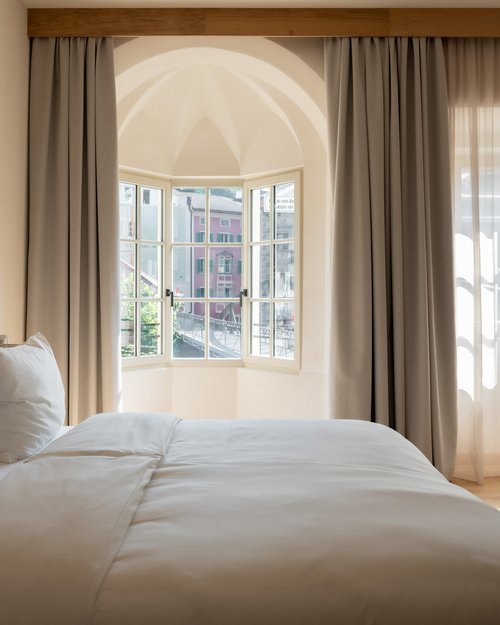 Camera da letto luminosa con letto grande, poltrona e finestra aperta con vista su case colorate