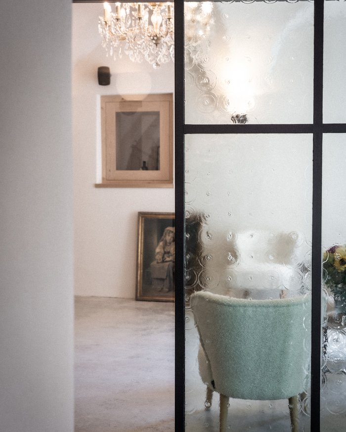 Vista attraverso una porta in vetro smerigliato su una stanza luminosa con poltrona e lampadario