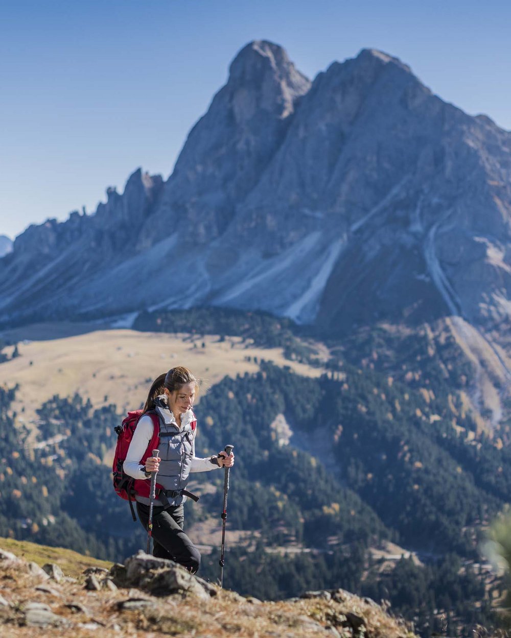 Donna escursionista con zaino e bastoncini in montagna con cielo sereno