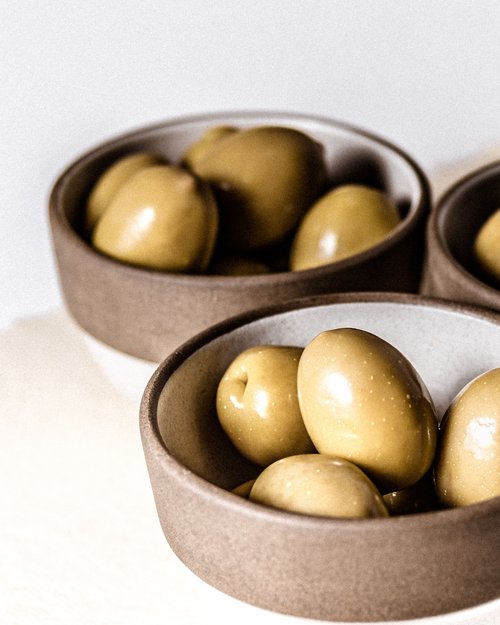 Olive verdi in ciotole di ceramica marrone su sfondo bianco