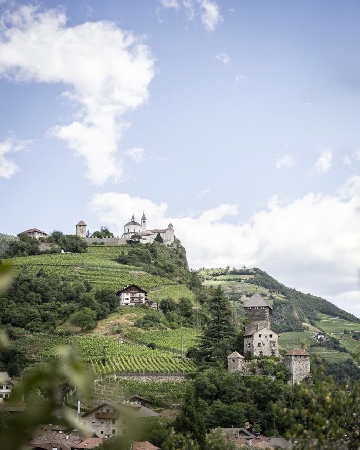 Paesaggio con vigneti, castello e chiesa su una collina sotto un cielo azzurro