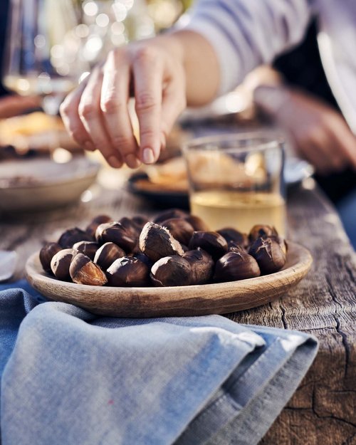 Mano prende castagne arrosto da ciotola di legno su tavolo rustico