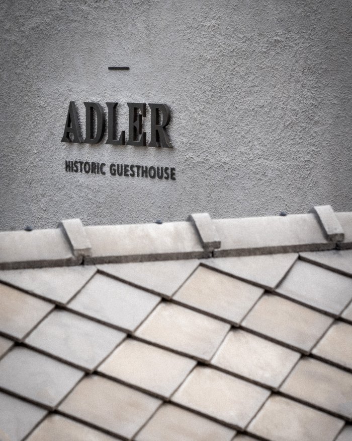 Scritta Adler Historic Guesthouse su muro grigio sopra tetto in tegole