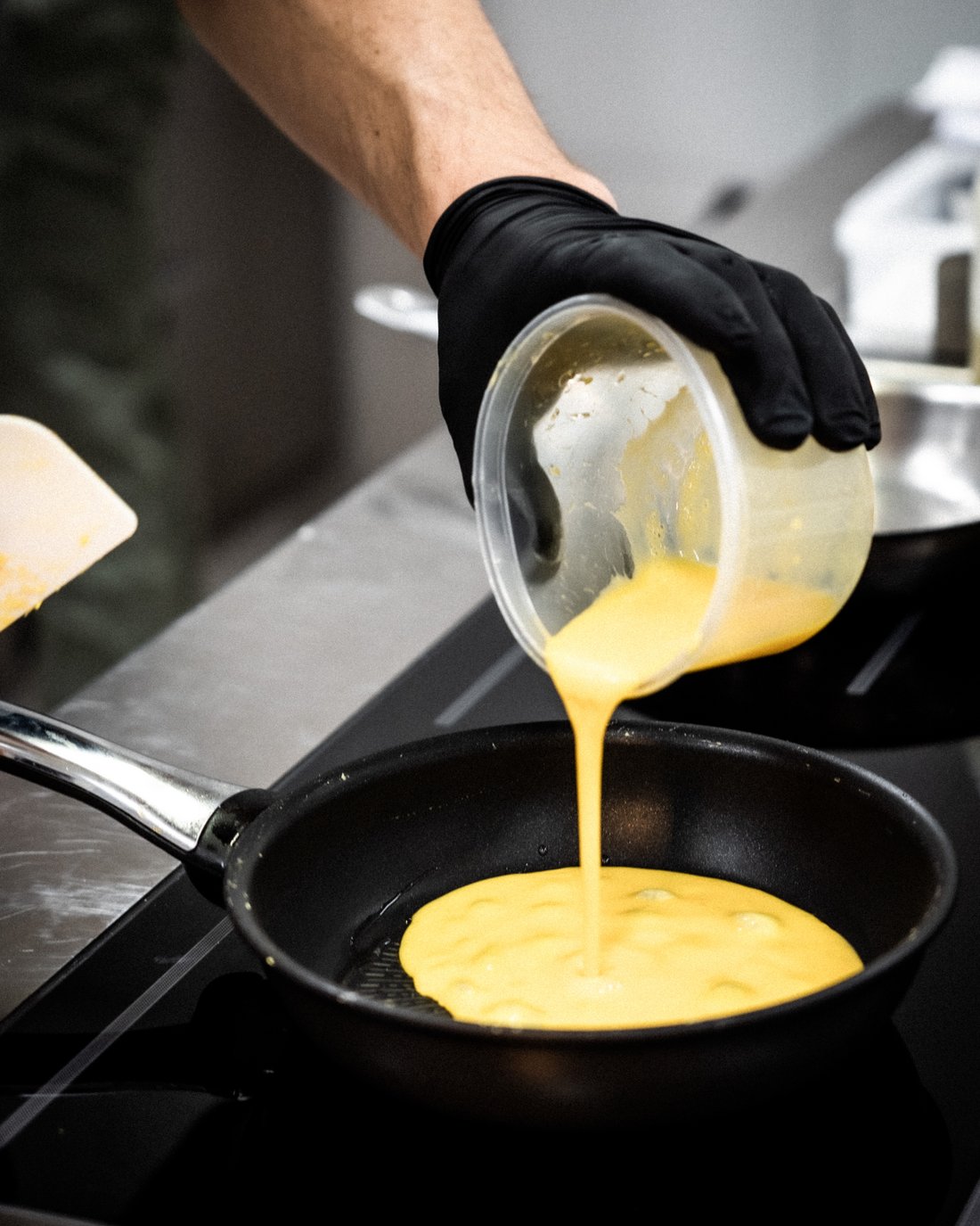 Persona versa uova sbattute in una padella per cucinare