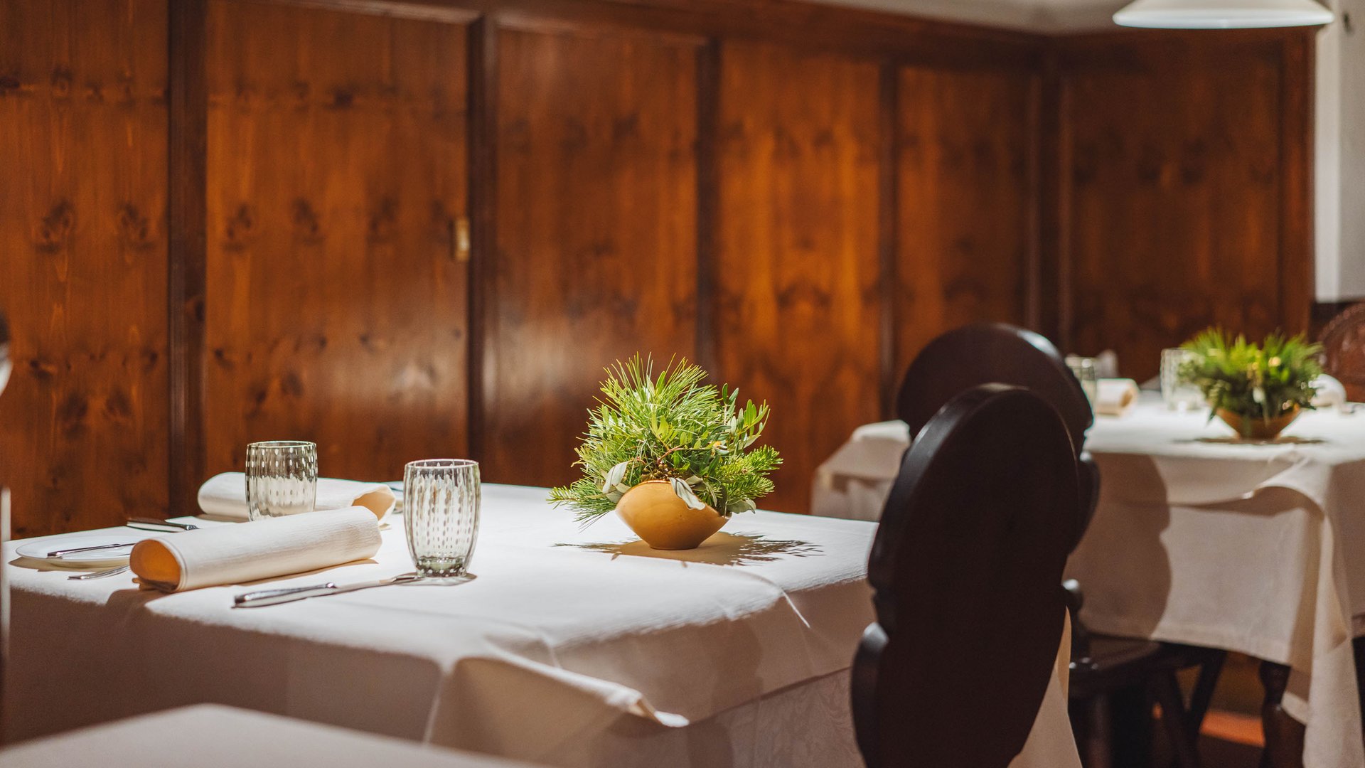 Tavoli di ristorante con tovaglie bianche e piante verdi in interno in legno