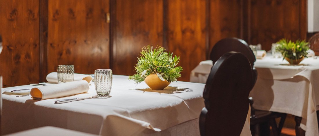 Tavoli di ristorante con tovaglie bianche e piante verdi in interno in legno