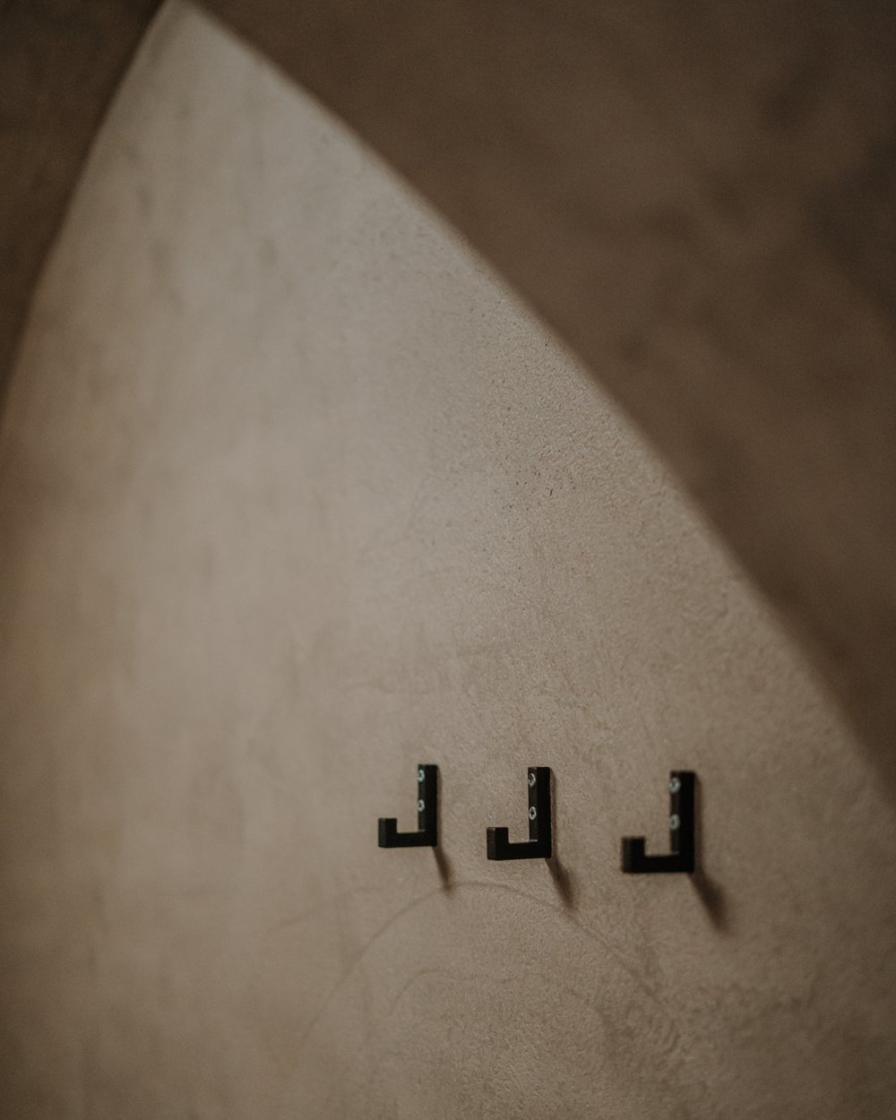 Tre ganci neri su una parete beige strutturata sotto un arco