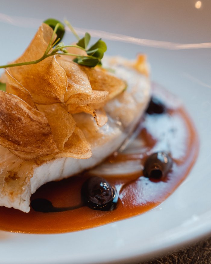 Pesce impiattato con patatine e salsa su piatto bianco