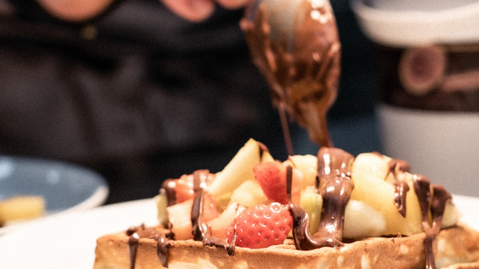 Mano versa salsa al cioccolato su waffle con frutta su piatto bianco
