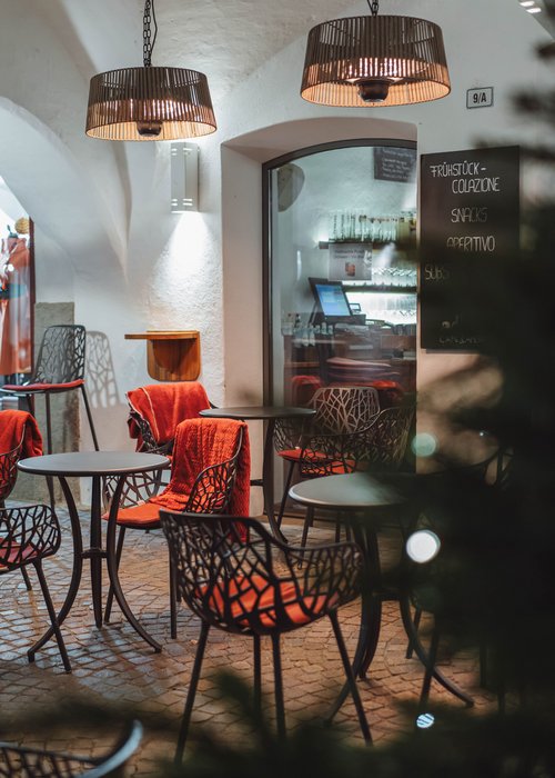 Area esterna vuota di un bar con tavoli, sedie e coperte rosse sotto lampade