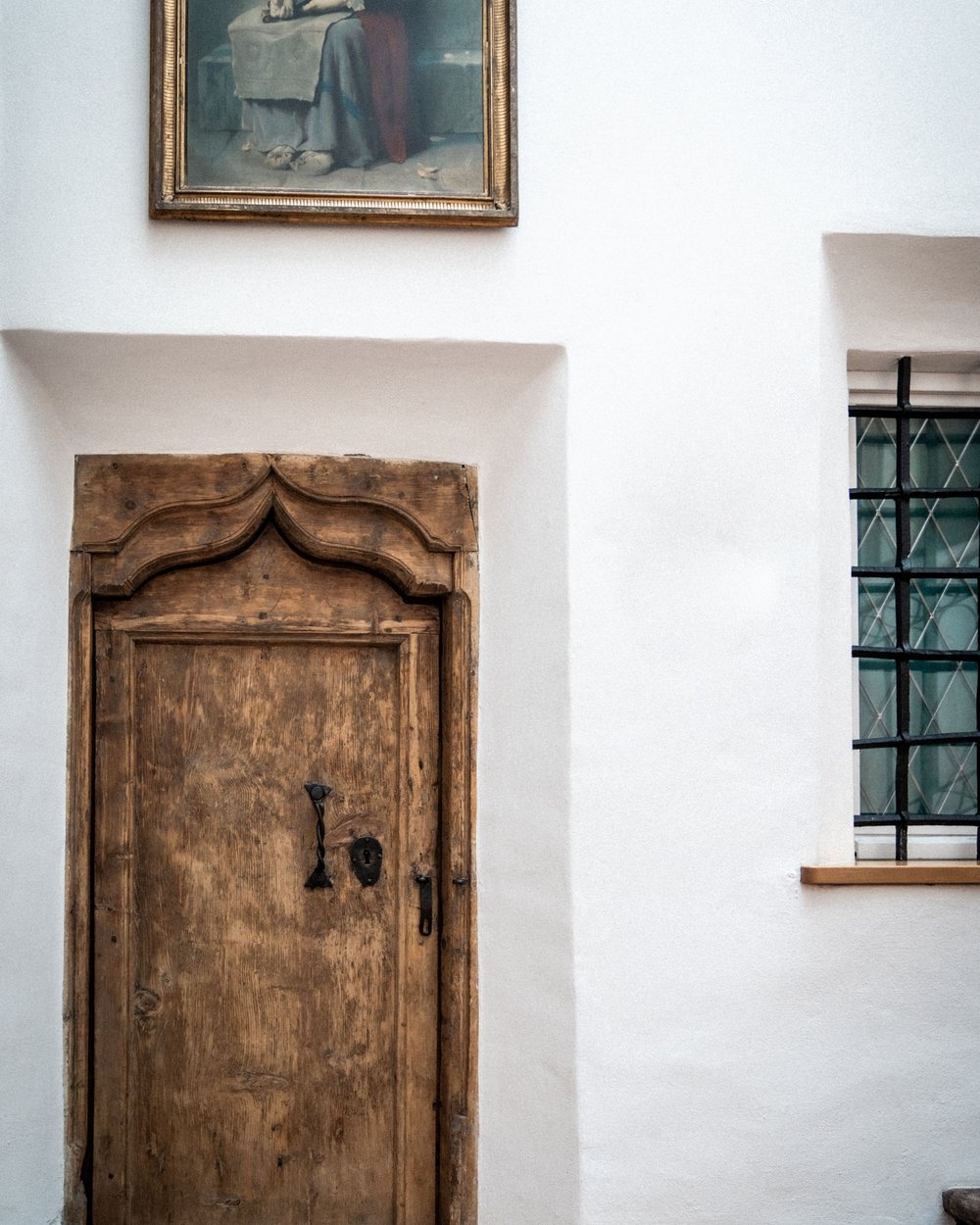 Porta in legno vecchia e decorata su parete bianca con dipinto sopra e finestra a lato