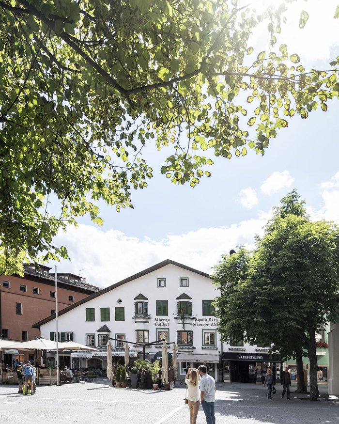 Coppia fotografa antico albergo sotto alberi verdi in piazza soleggiata