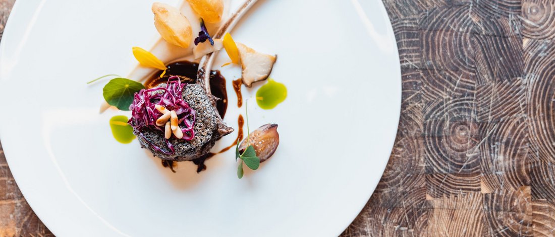 Piatto gourmet elegantemente impiattato con costolette di agnello e guarnizioni colorate