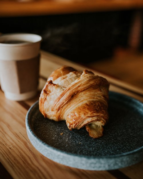 Cornetto fresco su un piatto grigio con caffè sullo sfondo