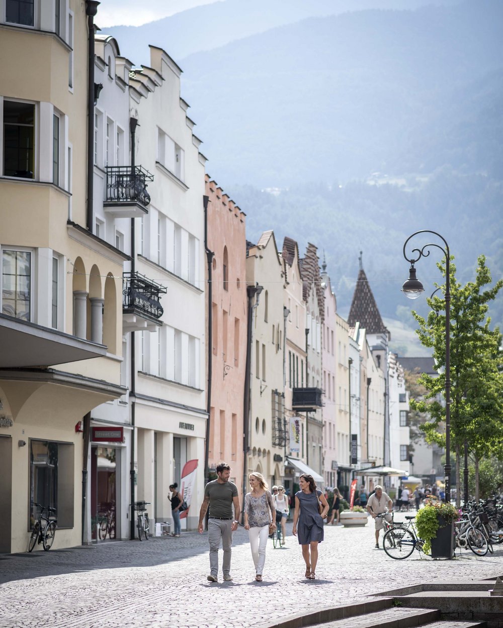 Persone che passeggiano in città alpina con case colorate e montagne sullo sfondo