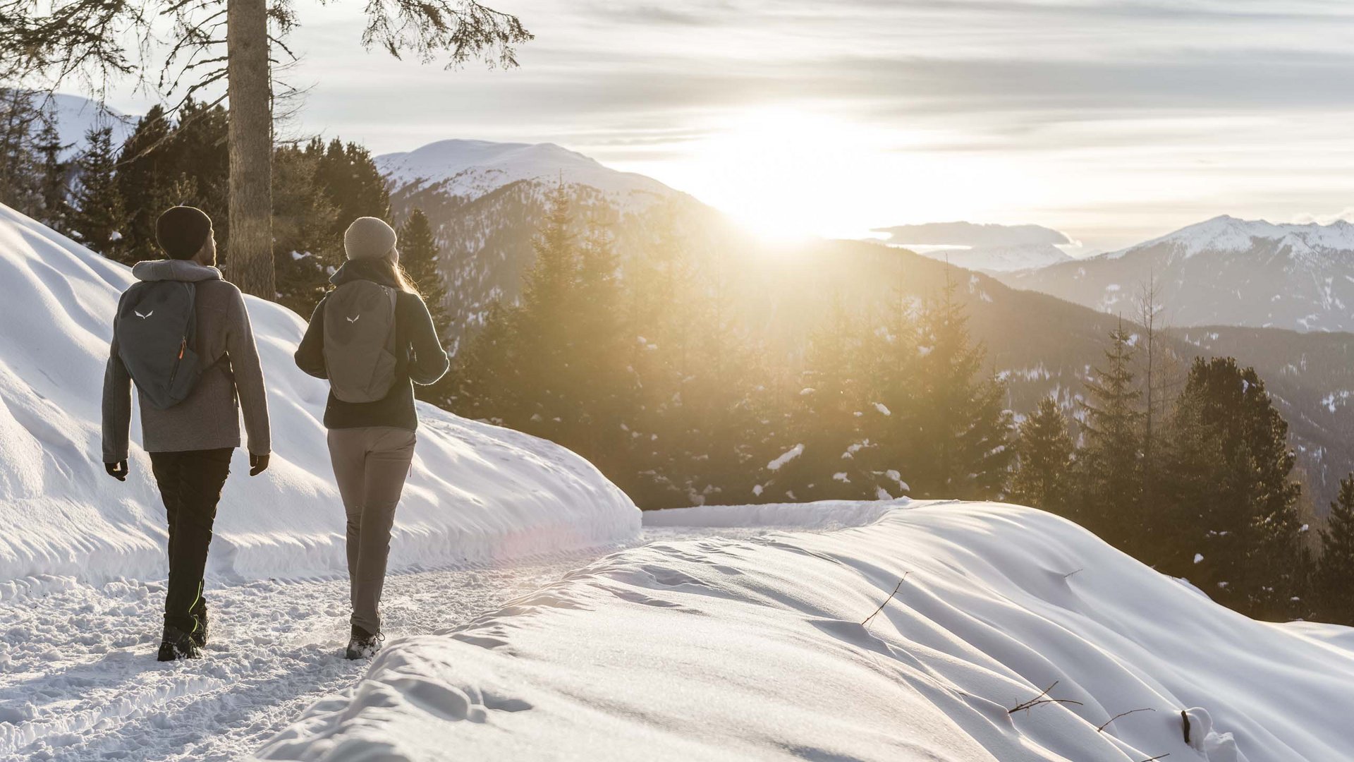 Due escursionisti camminano su sentiero innevato al tramonto in montagna