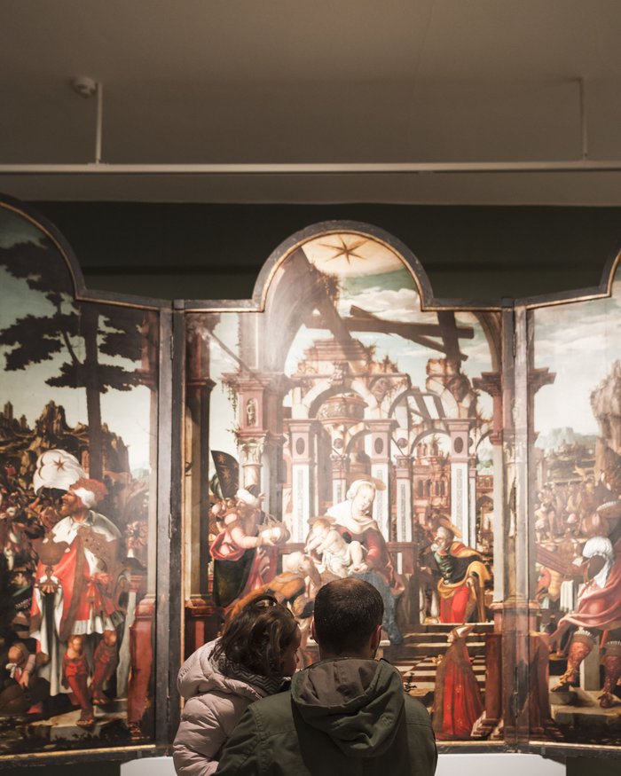 Un uomo tiene un bambino davanti a un dipinto rinascimentale in una galleria d'arte