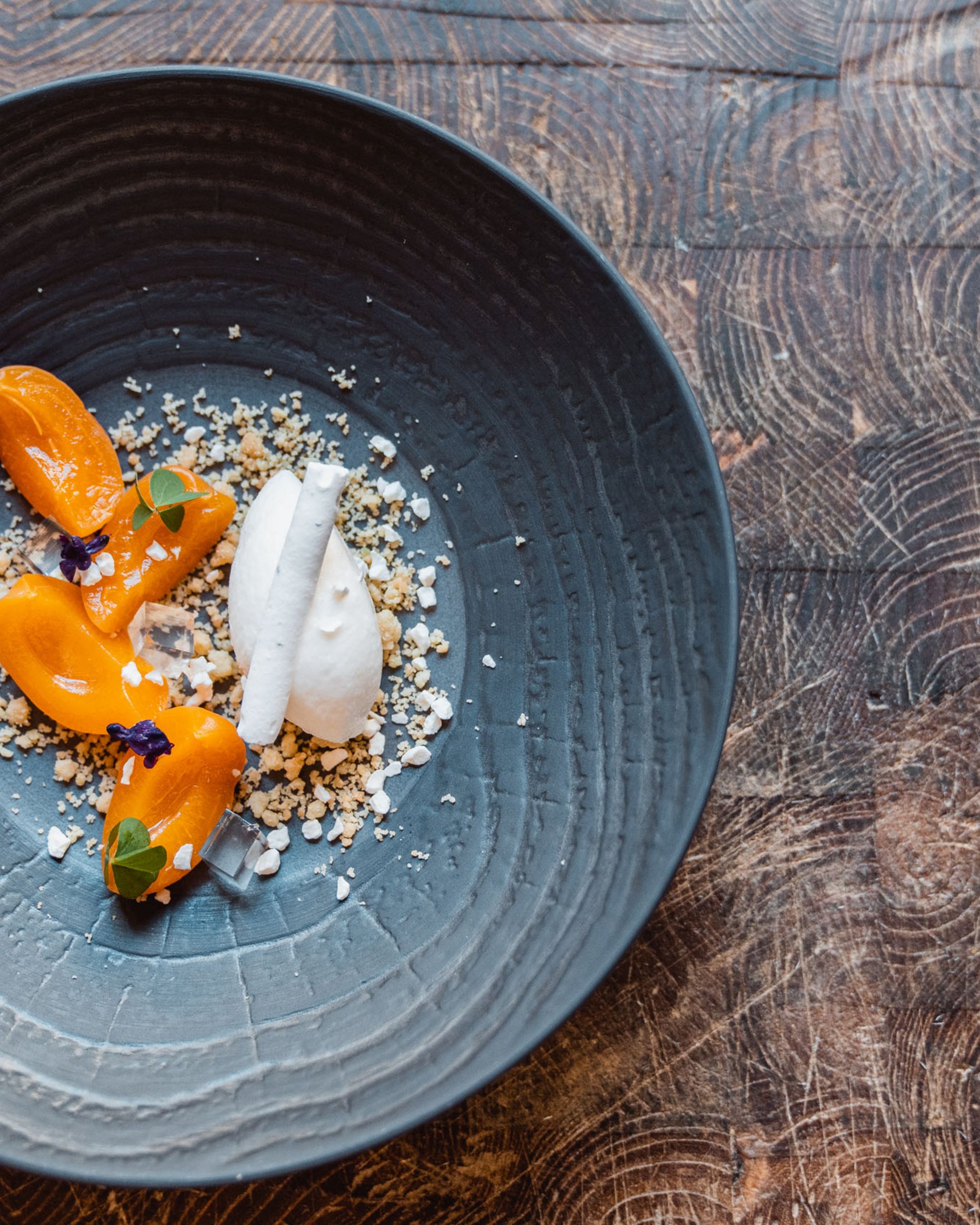 Dessert artisticamente impiattato con frutta arancione e crema bianca su piatto scuro