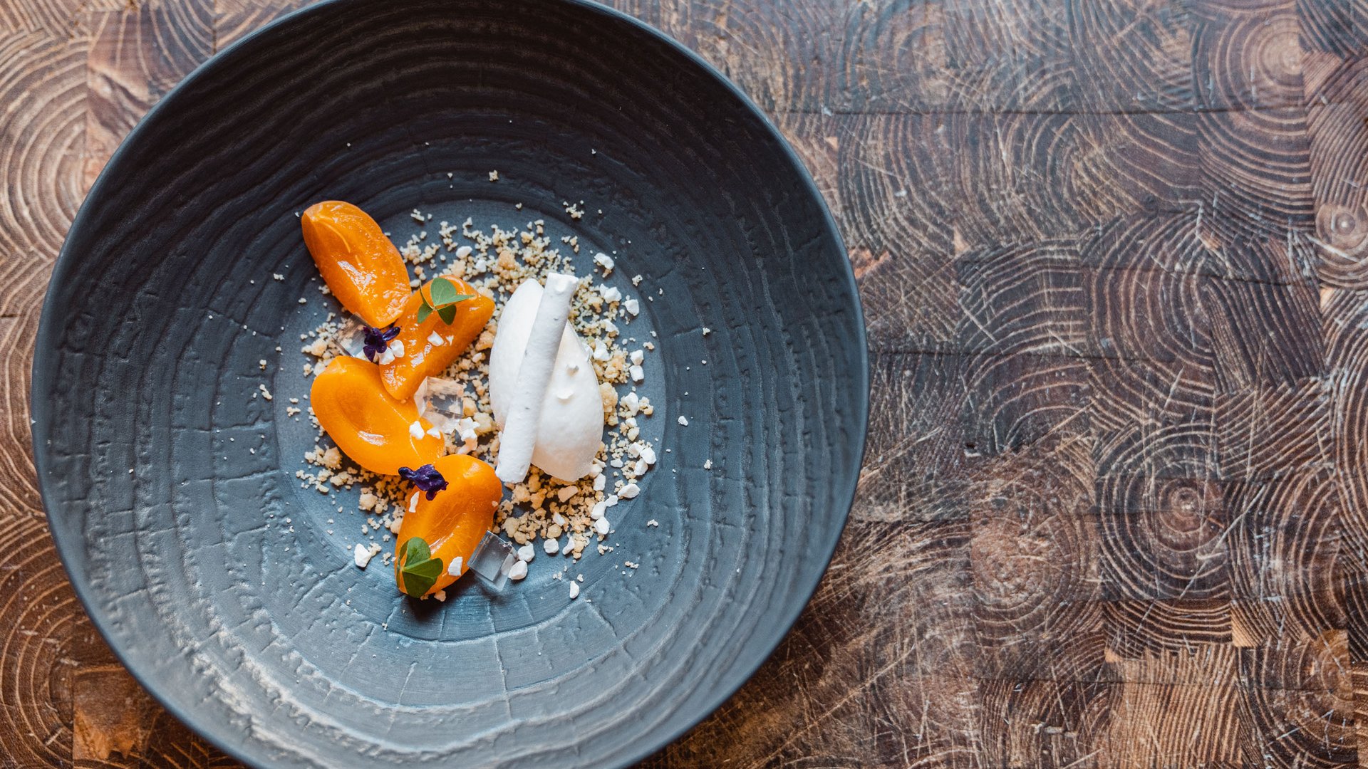 Dessert artisticamente impiattato con frutta arancione e crema bianca su piatto scuro