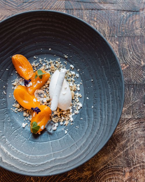 Dessert artisticamente impiattato con frutta arancione e crema bianca su piatto scuro