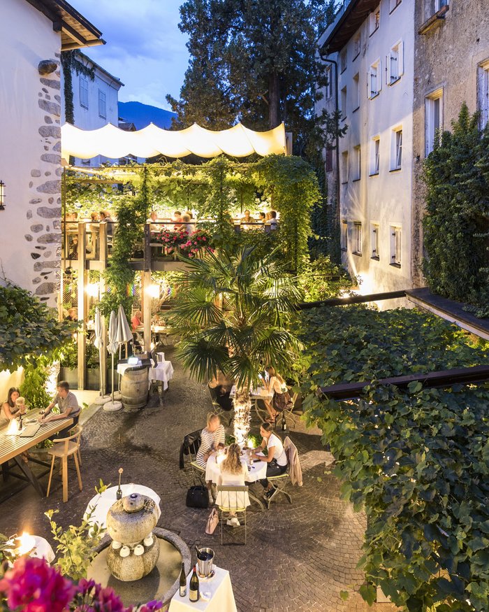 Terrazza serale di un ristorante con ospiti e piante in un vicolo